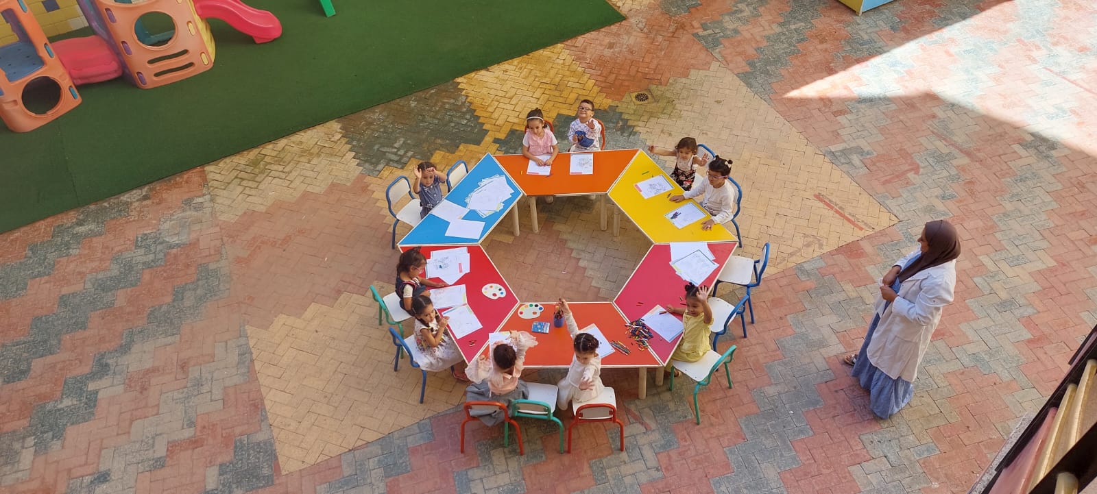 Élèves de maternelle en atelier de dessin autour d'une table hexagonale colorée