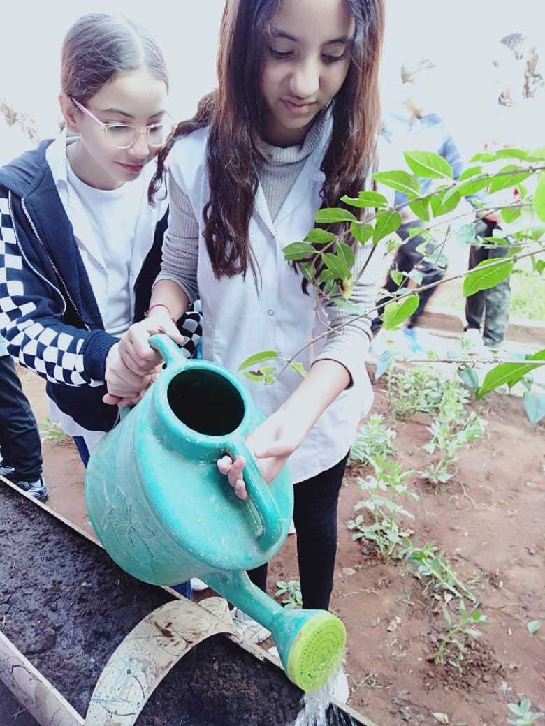Deux collégiennes arrosant une jeune plantation dans le jardin de l'école