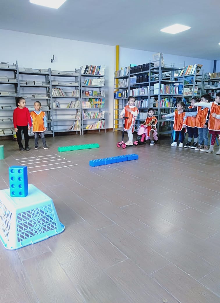 Enfants en parcours de motricité avec trottinettes dans la bibliothèque